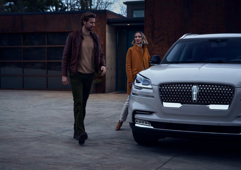 A man and a woman approaching a 2024 Lincoln Aviator® SUV, which illuminates certain lights when they are close | Doral Lincoln in Doral FL