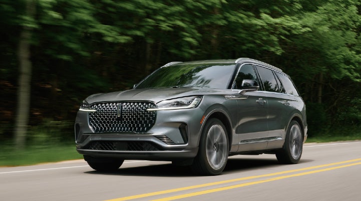 A 2027 Lincoln Aviator® SUV is being driven down a road lined with trees. | Doral Lincoln in Doral FL